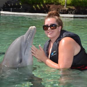 Person wearing a life vest interacting with a dolphin in shallow water